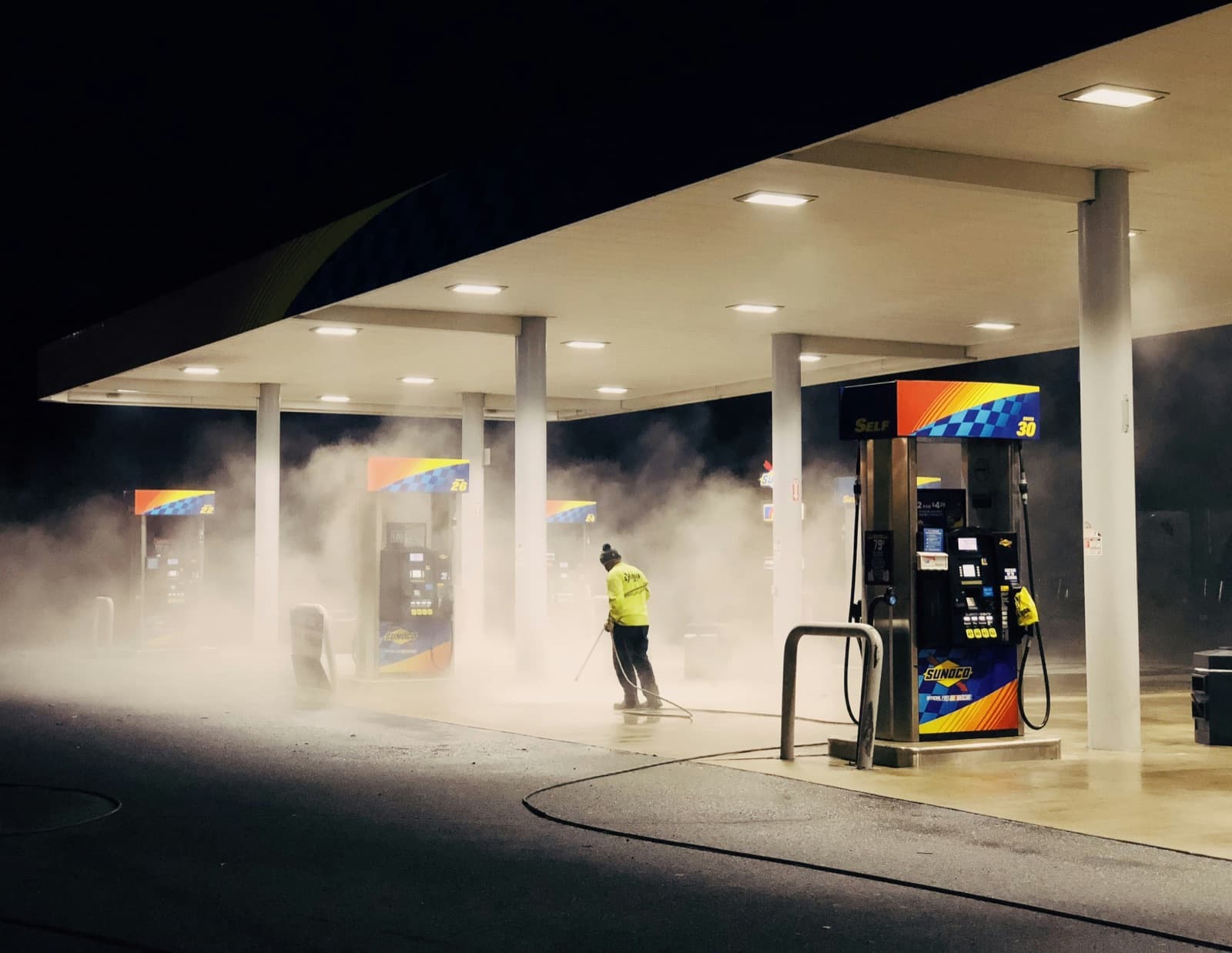 A pressure washing contractor cleaning a commercial gas station lot at night