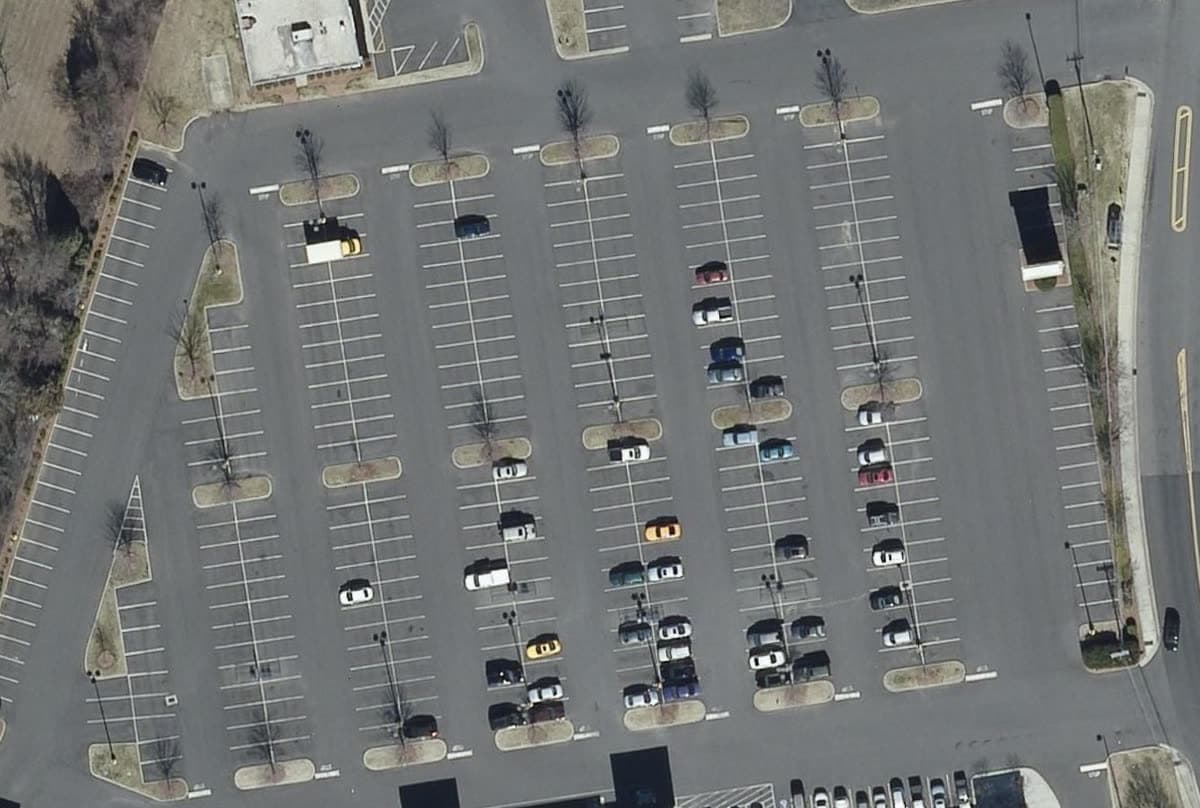 Aerial view straight down on a retail parking field, Feb 2015: Bright stall lines on gray pavement.
