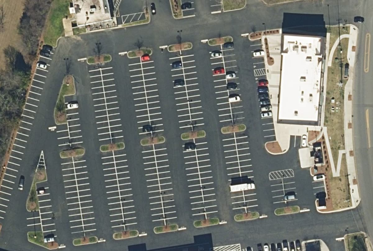 Aerial view straight down on a retail parking field, Feb 2023: Black pavement, every line repainted in a new layout, a new building on the east side.