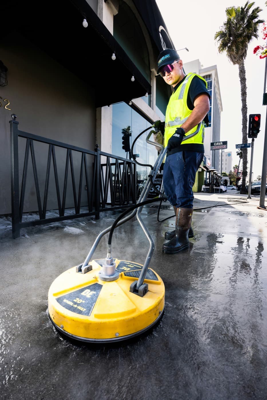 A contractor running a surface cleaner along a commercial storefront sidewalk