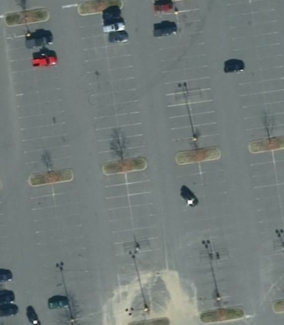 Aerial view straight down on parking rows in February 2019: gray pavement with stall lines faded to faint traces.