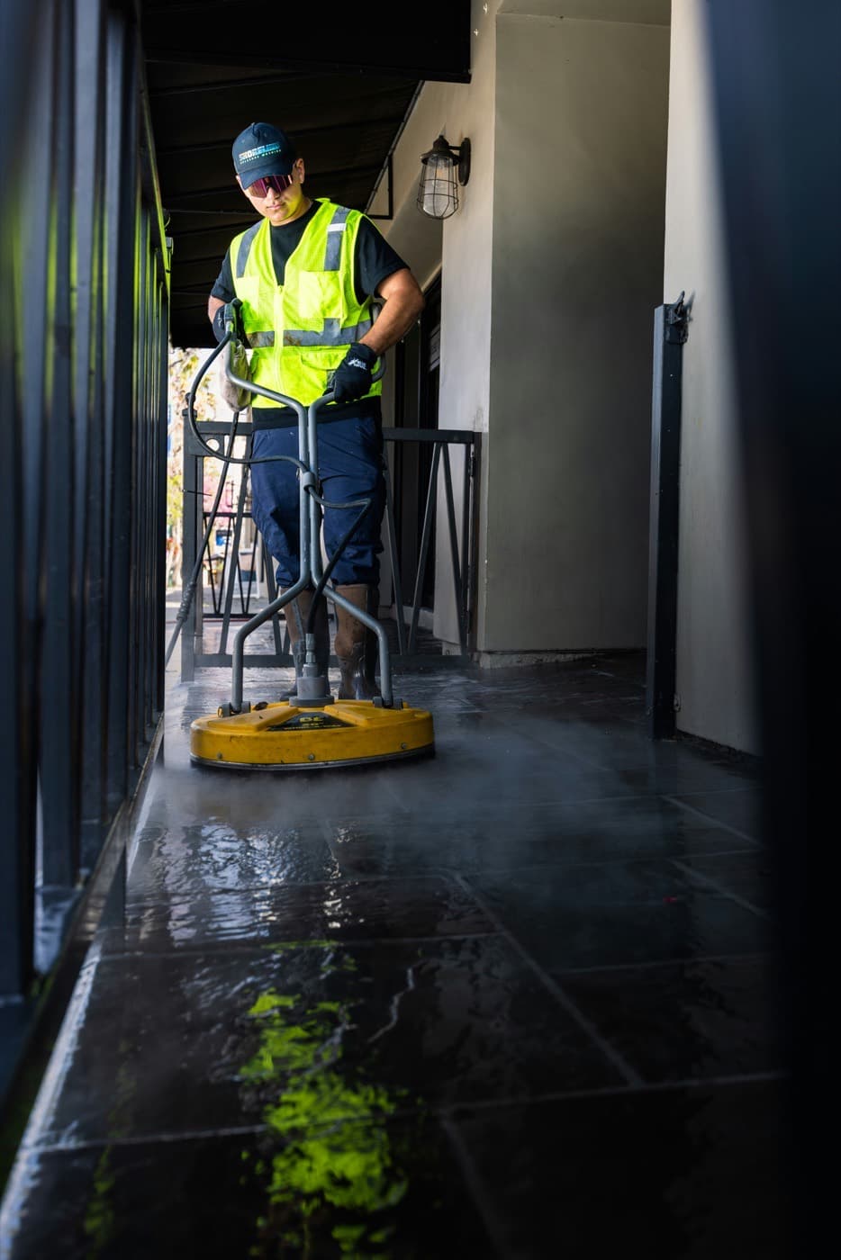A contractor running a surface cleaner along a covered commercial walkway