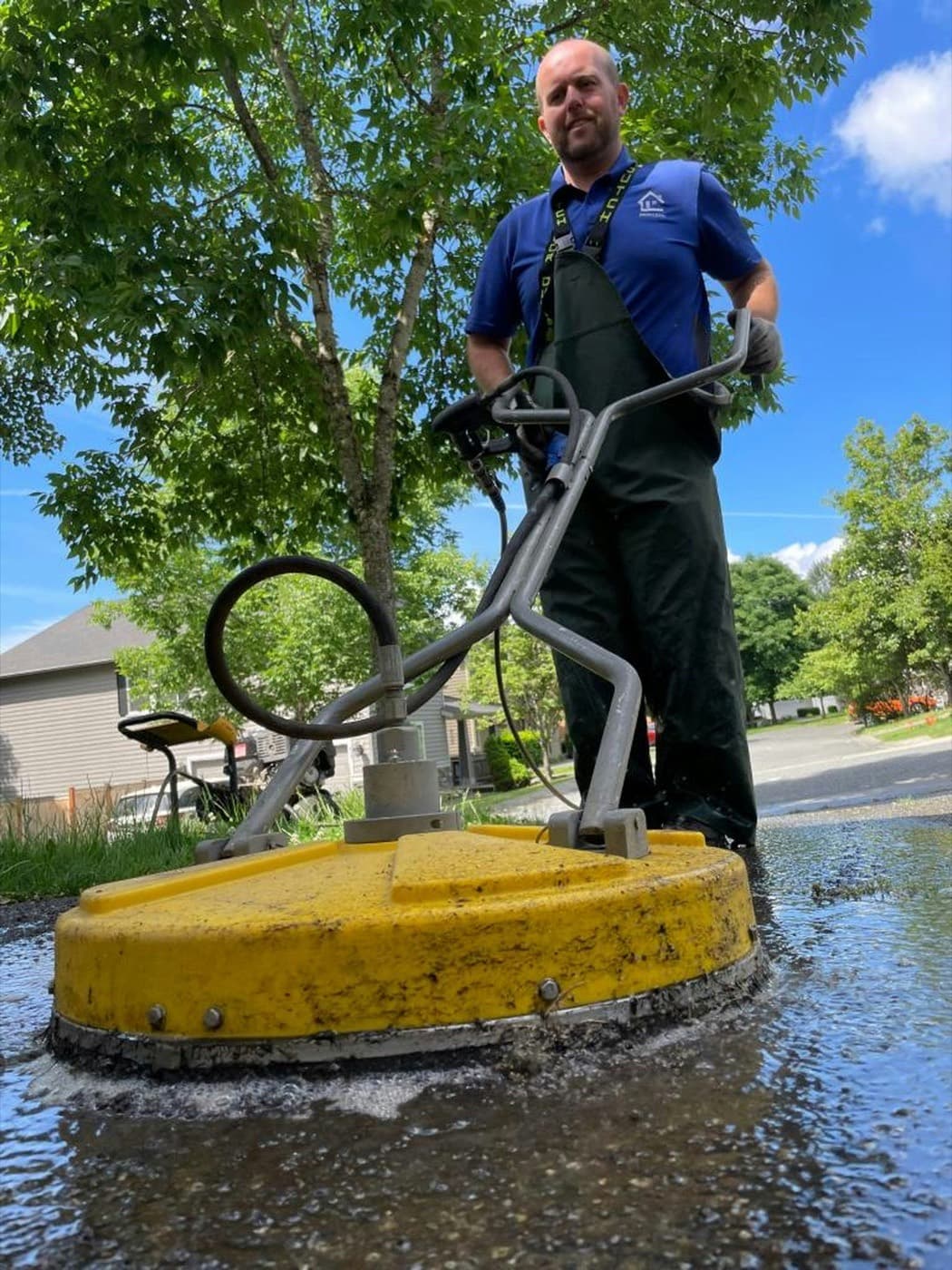 A contractor running a surface cleaner across a residential driveway on a clear day