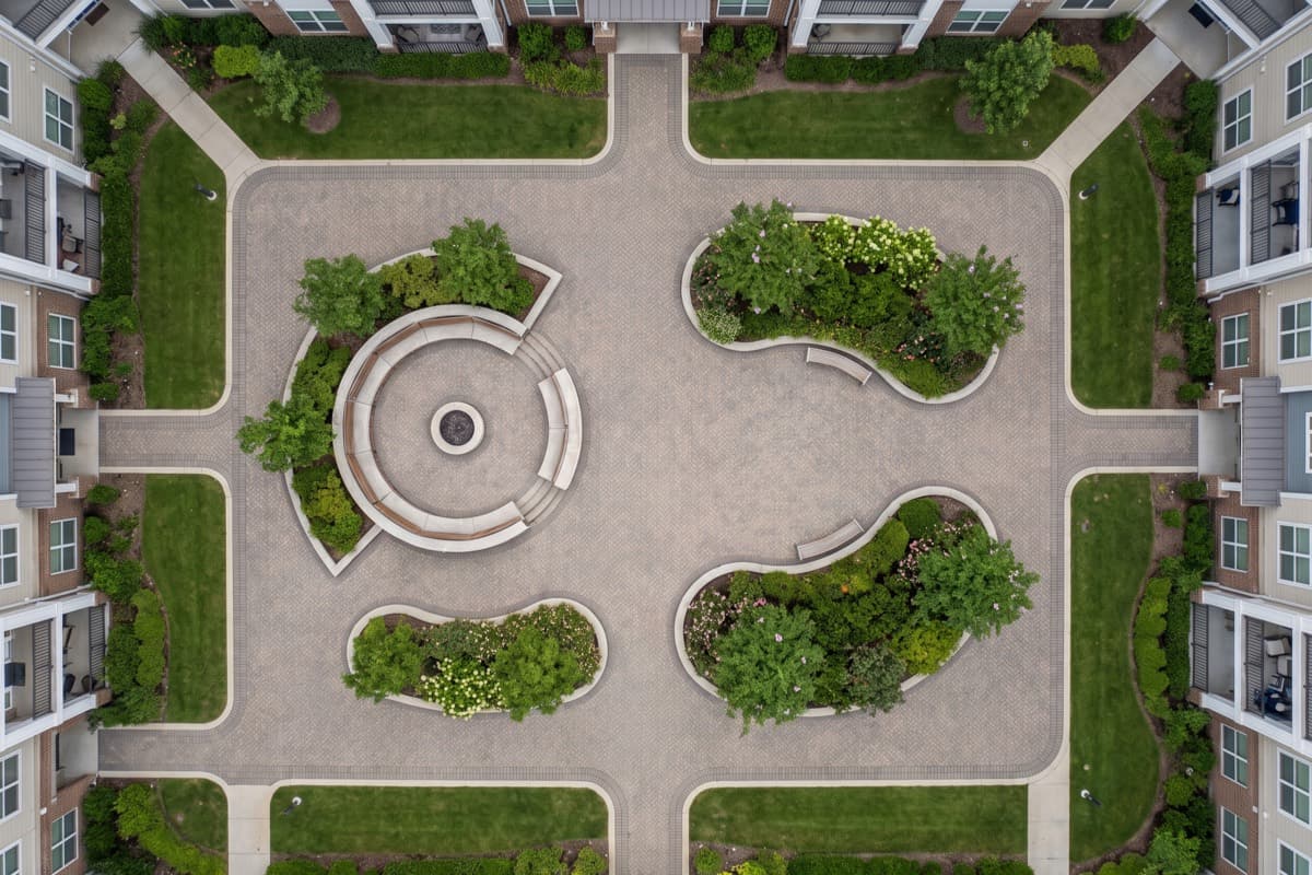 Overhead view of an interlocking paver courtyard at an apartment complex, the paving broken up by planters, a curved walkway and building edges