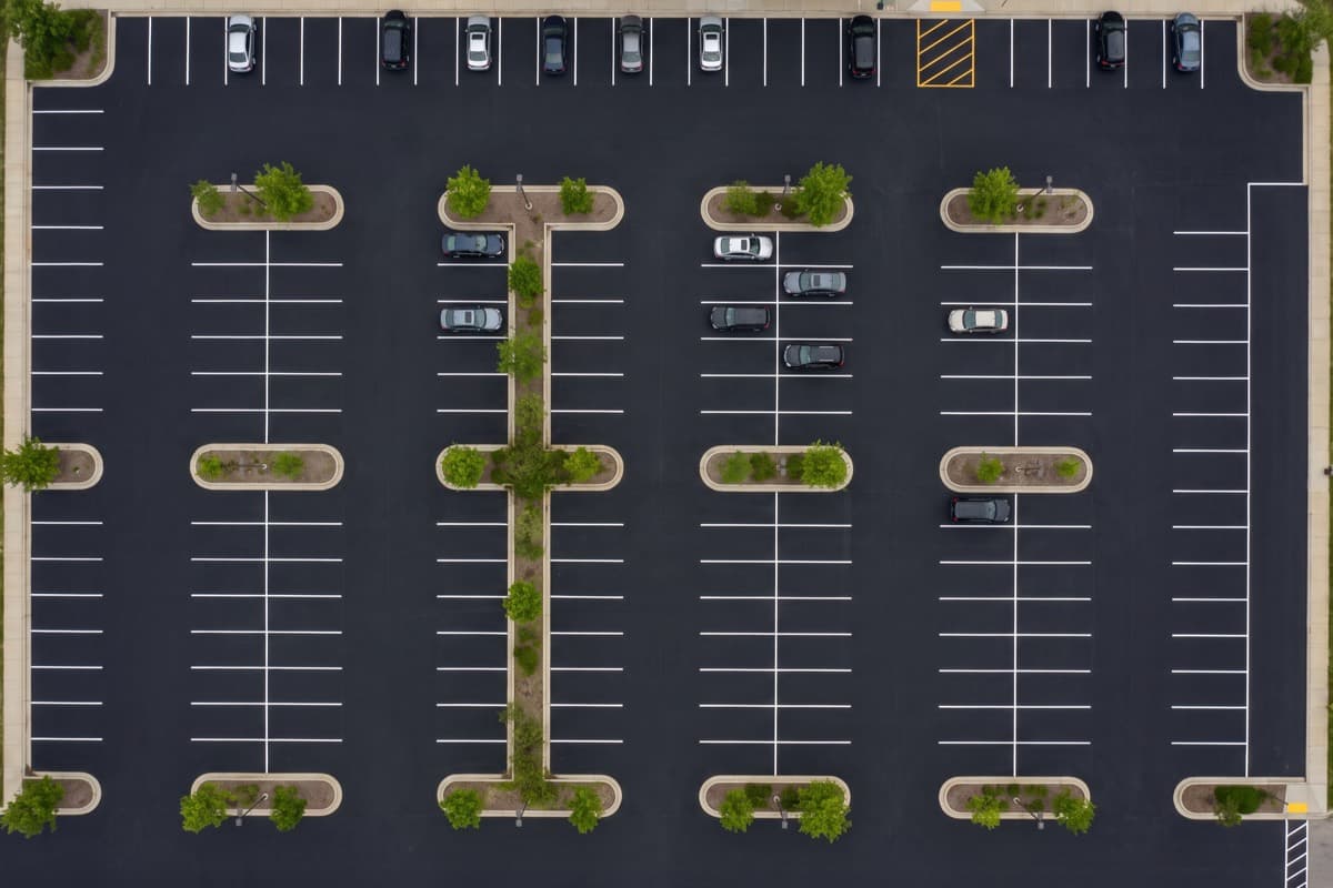 Overhead view of a freshly sealcoated retail parking lot with crisp white stall striping and landscaped curb islands