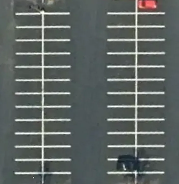 Aerial view straight down on two bays of a striped parking lot: rows of 90 degree stalls back to back on each side of a drive aisle.